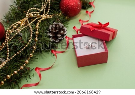 a white gold ring with a large stone in a red box on the background of a Christmas decor with bangs and red balls and a serpentine Royalty-Free Stock Photo #2066168429