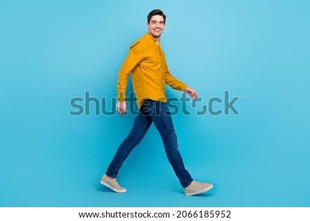 Photo of carefree worker guy move travel toothy smile wear yellow shirt jeans footwear isolated blue color background
