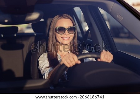 Photo of charming sweet young lady dressed white shirt dark eyewear smiling driving automobile outdoors urban route Royalty-Free Stock Photo #2066186741
