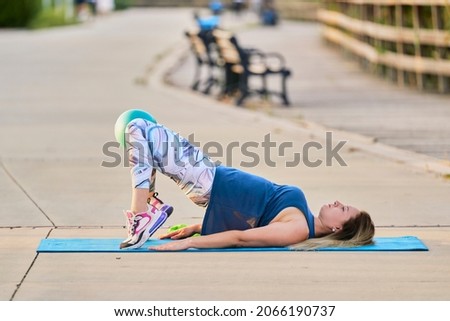 Young smiling woman doing fitness exercises in the park on the green grass with workout clothes