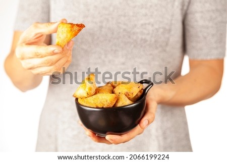 A woman is holding a porcelain bowl of Indian Samosas, triangular shaped crispy fried snacks with spicy, savory fillings. She is eating one. Light and airy photo