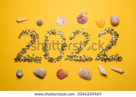 2022 New year text inscription card made of golden sequins and seashells on the yellow background.