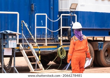 Action of a safety officer in orange coverall and white hardhat is walking around the work place for safety inspection. Industrial working people photo scene.