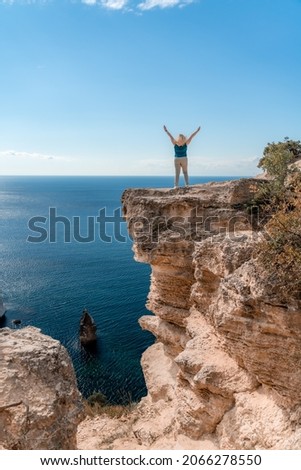 The woman at the top of the mountain raised her hands up on blue sky background. The woman climbed to the top and enjoyed her success. Back view.