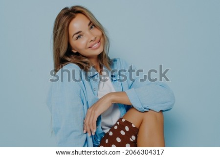 Adorable outgoing young woman with long hair and perfect healthy skin, smiling broadly at camera while sitting sideways, showing her straight white teeth. Beauty, style and fashion concept.