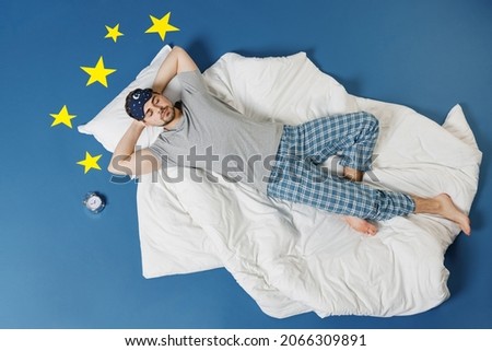 Full length top view calm young caucasian man in pajamas jam sleep mask rest relax at home lies in bed hold hands behind head neck isolated on dark blue sky background Good mood night bedtime concept Royalty-Free Stock Photo #2066309891