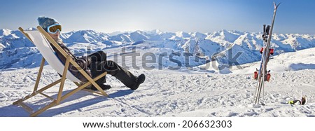 Panorama of a girl sunbathing in a deckchair near a snowy ski slope