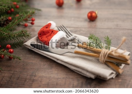 Fir branches and cutlery with Santa hat. table setting with Christmas decorations. Christmas table place setting. Christmas serving cutlery with napkin on wooden background.