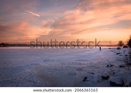 Winter sunset over the frozen sea. A silhouette of a woman walking on ice.