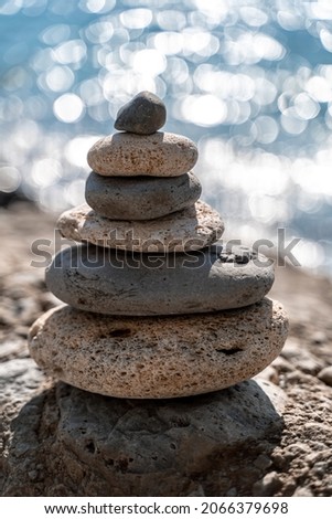 A tower of stones. Balanced pyramid of pebbles on the beach on a sunny day. Blue sea in the background. Selective focus, bokeh. Zen stones on the sea beach, meditation, spa, harmony, tranquility