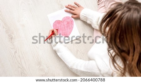 Little girl draws a red heart on the wooden floor. Top view. Copy space for text