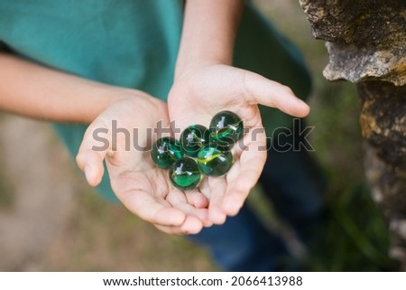 Close-up of green marble balls in hands. Child in green t-shirt showing green marbles at camera. Childhood, nature, fantasy concept