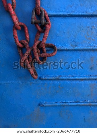 Photo of a red iron chain on a metal plate background with a blue color. There is a free space for writing suitable for use as a power point background or wallpaper.