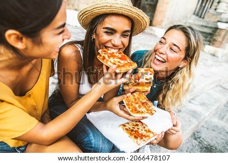 Three young female friends sitting outdoor and eating pizza - Happy women having fun enjoying a day out on city street - Happy lifestyle concept