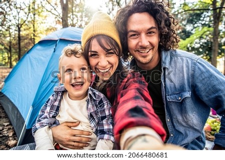 Happy family camping in the forest taking selfie portrait together - Mother, father and son having fun trekking in the nature sitting in front of the tent - Family, nature and trekking concept