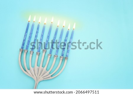 Image of jewish holiday Hanukkah with menorah (traditional candelabra) and candles over pastel blue background