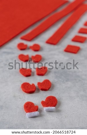 Making New Year's red felt mittens with a white stripe with your own hands. Blanks of felt, cozy little cut-out mittens. The concept of making Christmas toys and greeting cards. Vertical orientation.