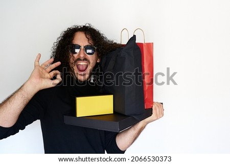 Black Friday sale concept where young smiling man with sunglasses picks up all his shopping bags and packages and makes ok sign