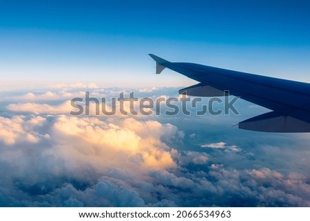 Flying and traveling, view from airplane window on the wing on sunset time. Aircraft wing under the earth and clouds. Flight in sky. Looking over aircraft wing in flight.  Royalty-Free Stock Photo #2066534963