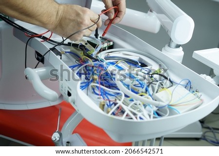 The master checks the electrical circuit in the faulty dental chair with a tester device. Repair of medical equipment.
