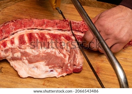 A man with a metal saw cuts meat. How to cut meat with metal saw at home. Royalty-Free Stock Photo #2066543486