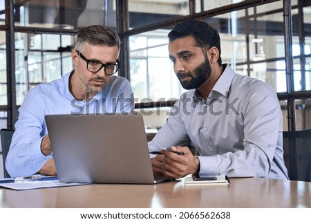 Two diverse business men analysts partners talking, working together, discussing data management using laptop computer. Indian manager consulting client with online technology at office meeting. Royalty-Free Stock Photo #2066562638