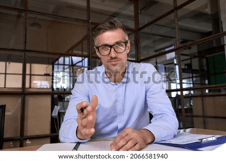 Happy caucasian businessman in glasses talking to camera at work by video call conference. Financial advisor executive consulting client remotely online in modern office looking at camera. Webcam view Royalty-Free Stock Photo #2066581940