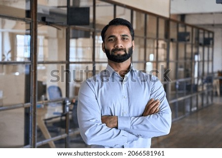 Confident happy successful ceo financial manager. Bearded indian businessman looking at camera standing in modern office with arms crossed. Handsome classy corporation owner. Business portrait. Royalty-Free Stock Photo #2066581961