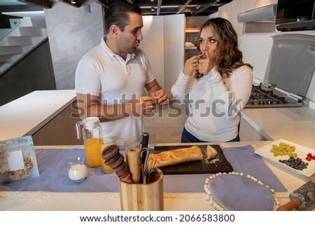 Happy latin couple having breakfast in their home kitchen drinking orange juice and eating bread