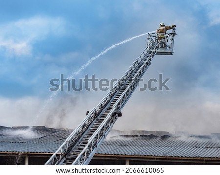 Firefighter on mechanized tower. Fire extinguishing with use of special equipment. Fire truck telescopic tower. Firefighter pours water on roof of building. Firefighter on tower on background of sky