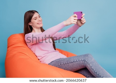 Profile side photo of young girl sitting in beanbag chair make selfie smartphone comfort isolated on blue colored background