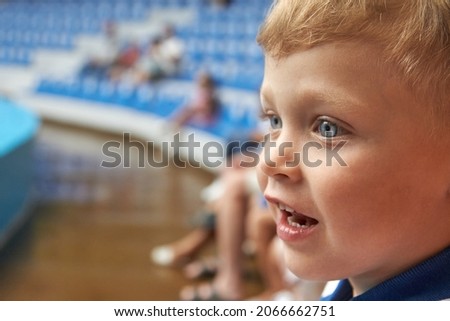 Happy blue-eyed boy watching the performance in dolphinarium in half empty auditorium