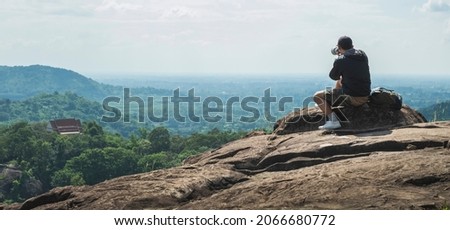 Photographer holding a camera photographing the landscape on a high cliff. travel concept Outdoor adventure and lifestyle