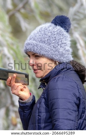 young latin girl in winter talking on her smartphone wearing a woolen hat, pearl earrings and a padded coat
