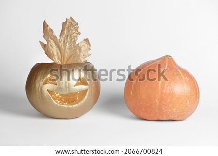Carved scary smiling pumpkin painted in gold color and organic are on a grey background. The concept of Halloween handmade decorations. 