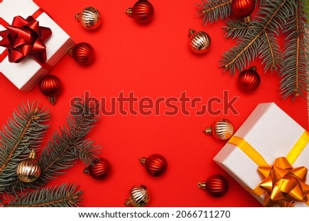  Christmas decorative composition with fir branches, gift boxes, golden and red christmas balls on red background. Christmas or New Year concept. Festive background with baubles and copy space.       
