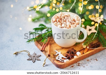 Cup of hot cocoa with marshmallows and candy canes on wooden table with christmas tree and glowing garland for christmas.
