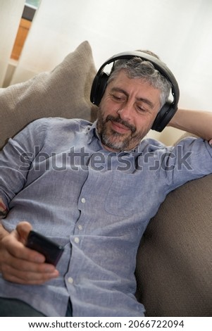 50 years old happy man listening to music and relaxing in a grey sofa