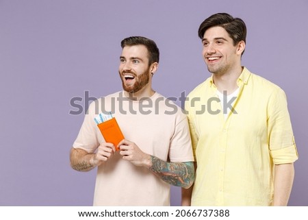 Two traveler tourist men friends in t-shirt tattoo translate fun hold passport ticket look aside isolated on purple background. Passenger traveling abroad weekends getaway. Air flight journey concept