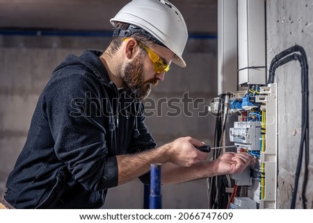 A male electrician works in a switchboard with an electrical connecting cable. Royalty-Free Stock Photo #2066747609