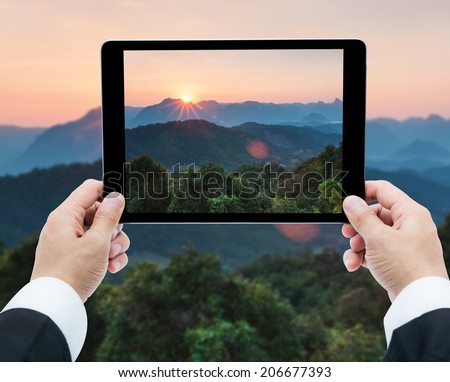 Businessman hands tablet taking pictures Majestic sunset in the mountains landscape at National mother Thailand