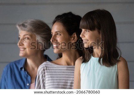 Happy daughter and granddaughter kid posing with mom and grandma, standing in row, looking away, smiling. Three Latin family female generations, 7s girl, young, senior women portrait Royalty-Free Stock Photo #2066780060