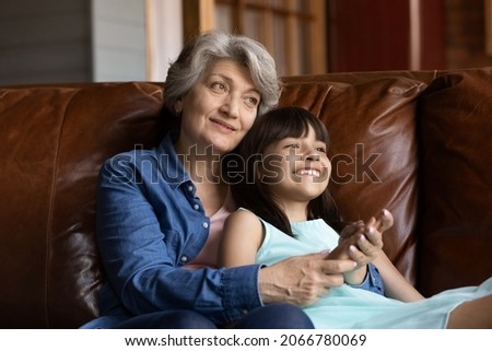 Happy grandmother hugging grand kid on couch at home, holding 7s girl in arms. Grey haired senior grandma enjoying leisure time with laughing cute granddaughter, talking to child. Family relations Royalty-Free Stock Photo #2066780069