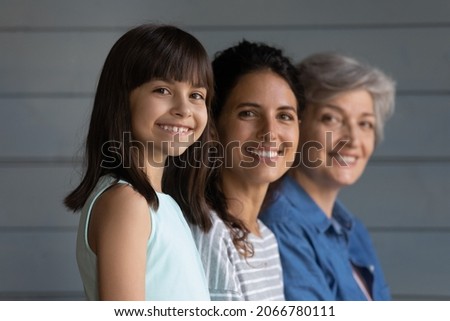 Happy three female family generations portrait. Joyful grand daughter girl, young grownup mother, senior grandmother standing in row, looking at camera, smiling, posing together at grey wall Royalty-Free Stock Photo #2066780111