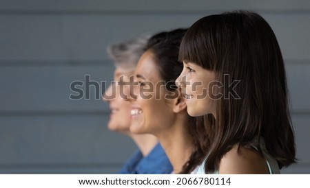 Happy cute 7s girl standing in line with young mother and senior grandmother, looking forward, thinking of future. Intergenerational family portrait with three female generations, dynasty, heredity