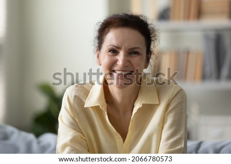 Head shot portrait of happy beautiful middle aged woman sitting on comfortable sofa looking at camera, enjoying free leisure weekend time alone at home or holding video call distant meeting. Royalty-Free Stock Photo #2066780573