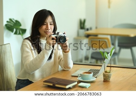Smiling young woman holding camera and checking picture previews.