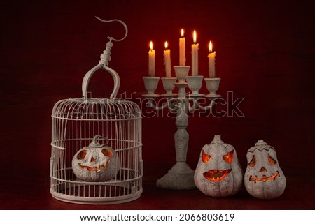 A funny white pumpkin like a head with carved eyes and a smiles with white candles and cage on a red background for the Halloween party