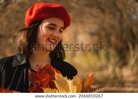 A Teengirl in a red beret with a bouquet of autumn leaves in her hands walks through the autumn forest. Autumn mood and concept.