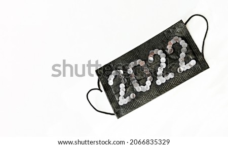Black medical face protective mask with new year 2022 numbers made of sequins on a white background close-up Healthy New Year concept copy space